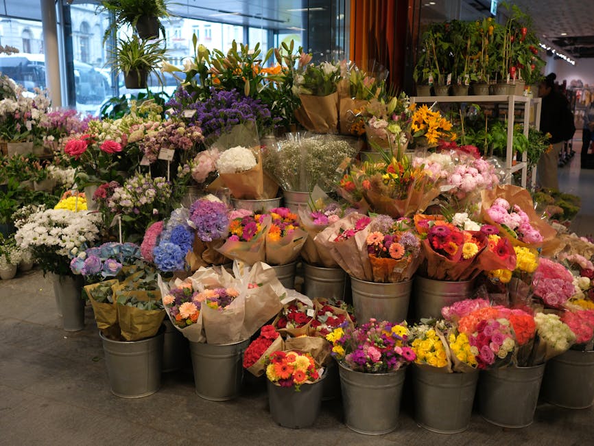A vibrant display of fresh floral bouquets arranged in metal buckets inside a florist shop. The collection includes a variety of flowers such as pink and white roses, purple lavender, yellow sunflower